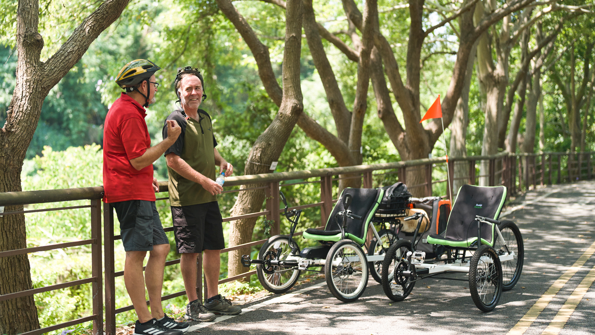 Two riders with their OVELOX recumbent trikes resting along a tree-lined path
